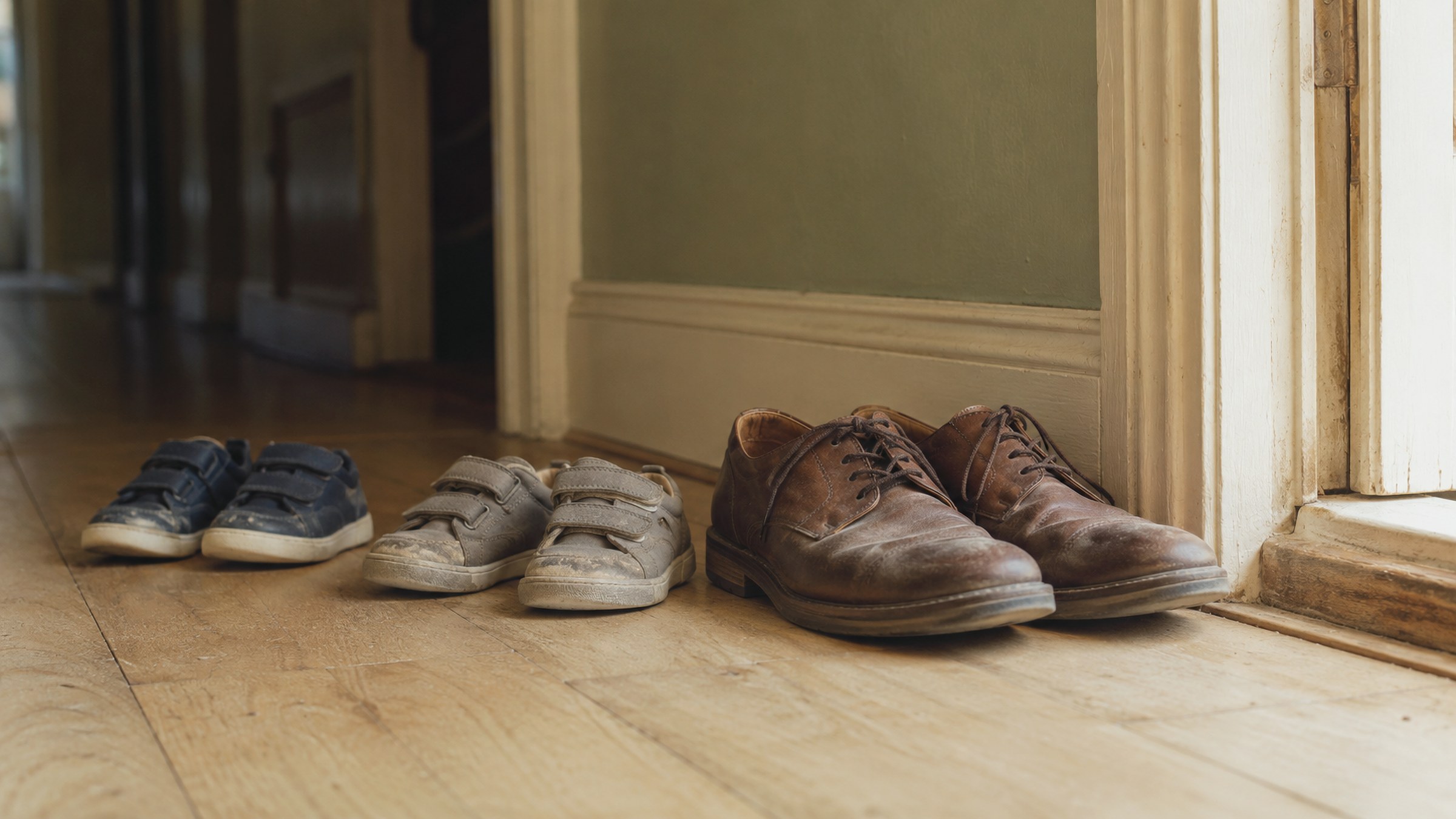 Zapatos de niños y adulto junto a la puerta de un hogar